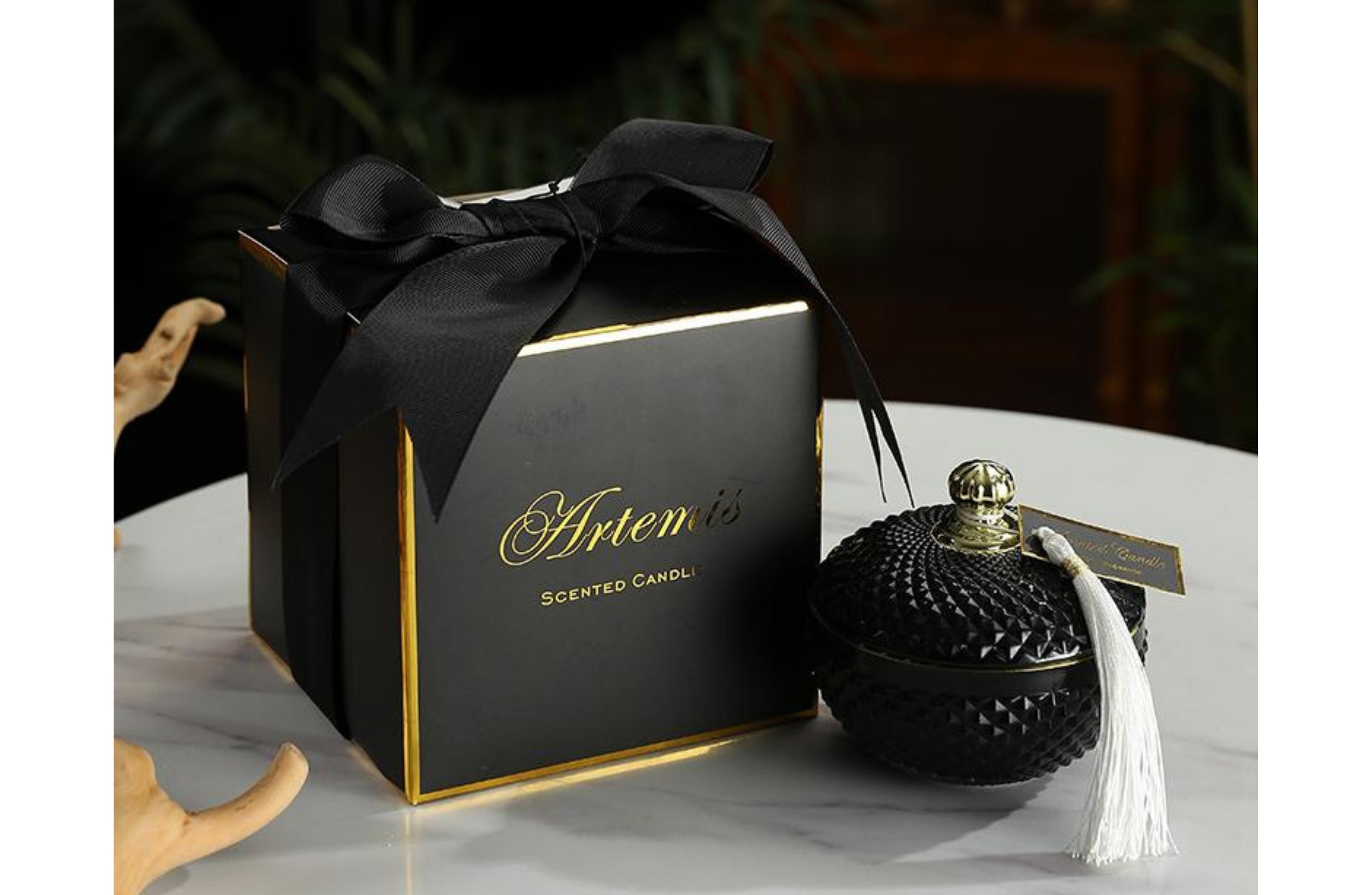 Artemis luxury candle in a textured black glass jar with tassel lid, scented with vanilla caramel, presented in a black and gold gift box.