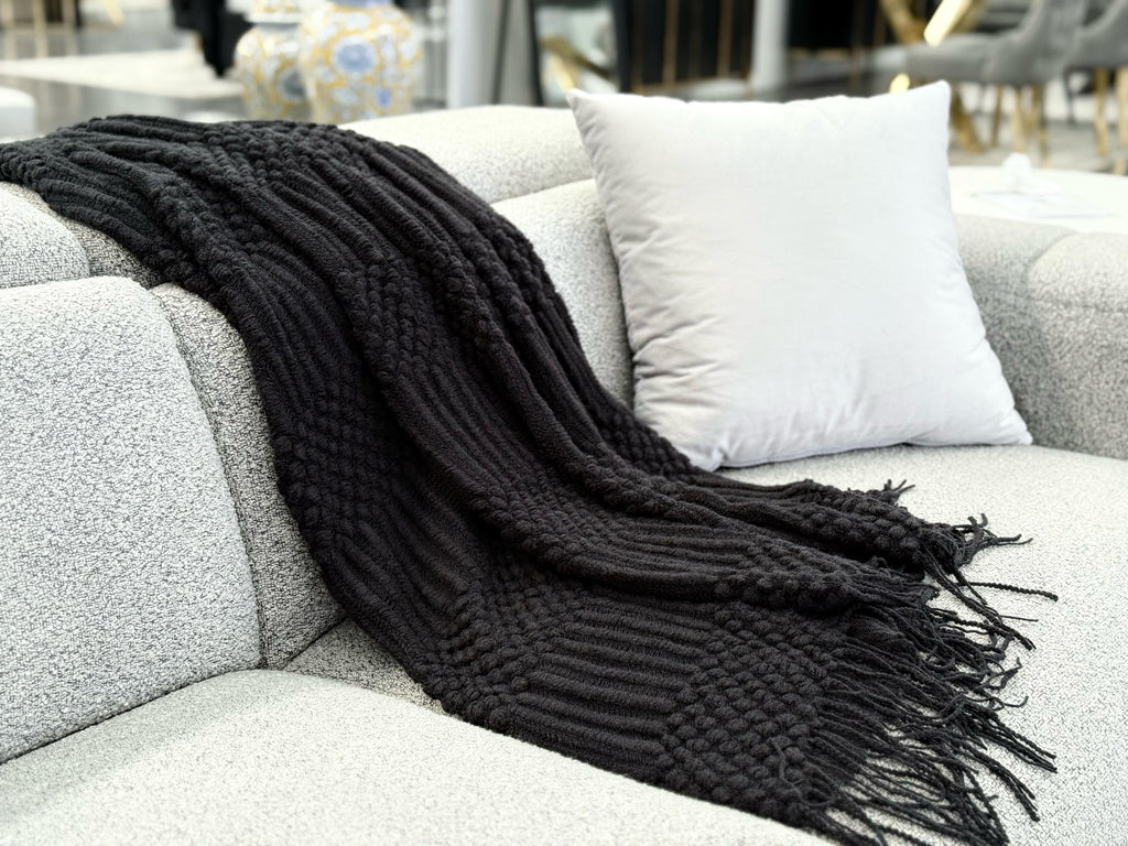 Black Tessa throw rug blanket styled over a grey sofa with a modern and elegant look.