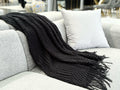 Black Tessa throw rug blanket styled over a grey sofa with a modern and elegant look.