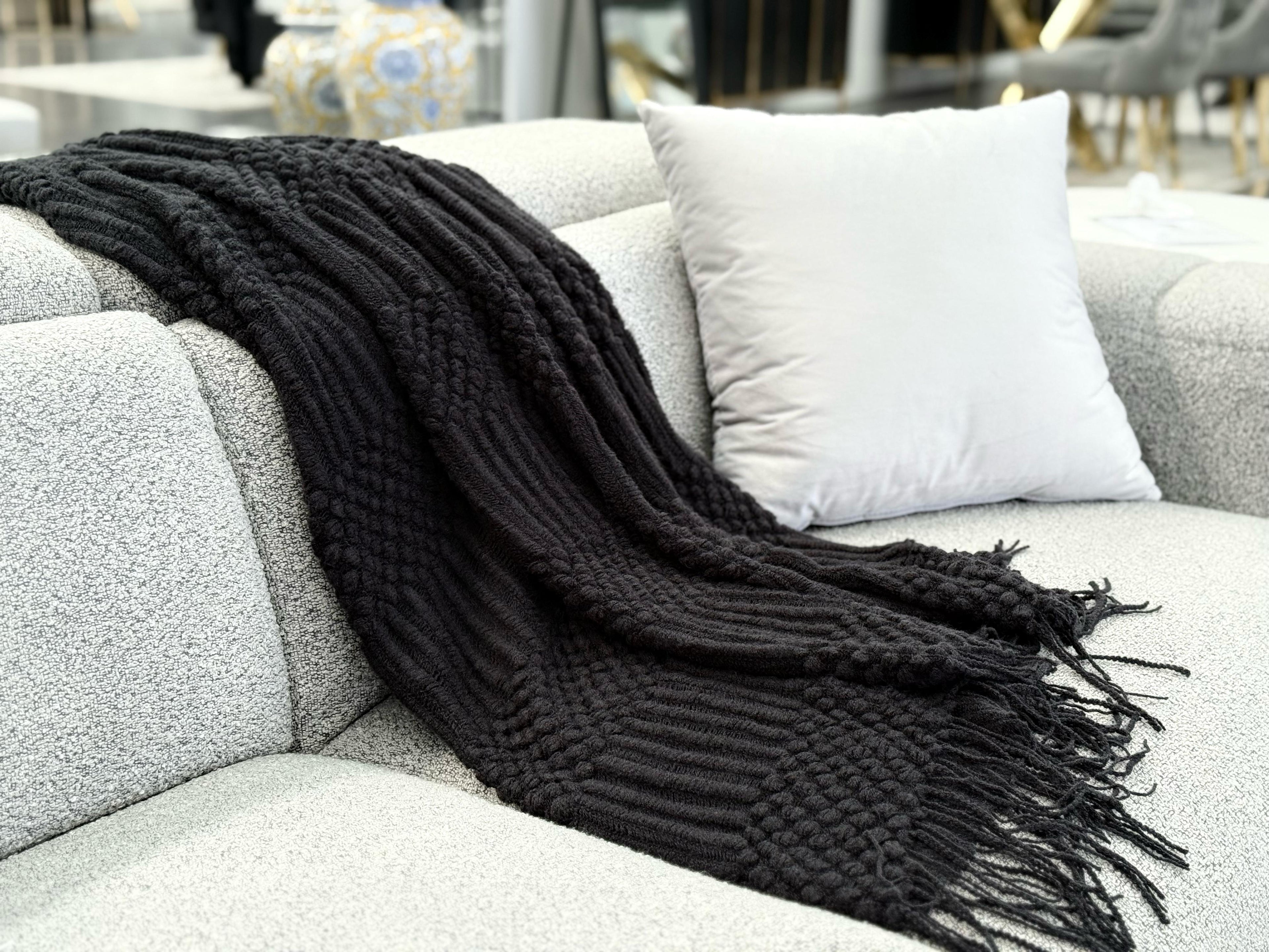 Black Tessa throw rug blanket styled over a grey sofa with a modern and elegant look.