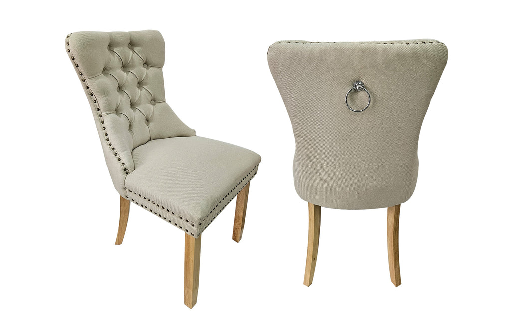 Set of 2 Alsea beige upholstered dining chairs with tufted back, stud trim, ring handle, and rubberwood legs.