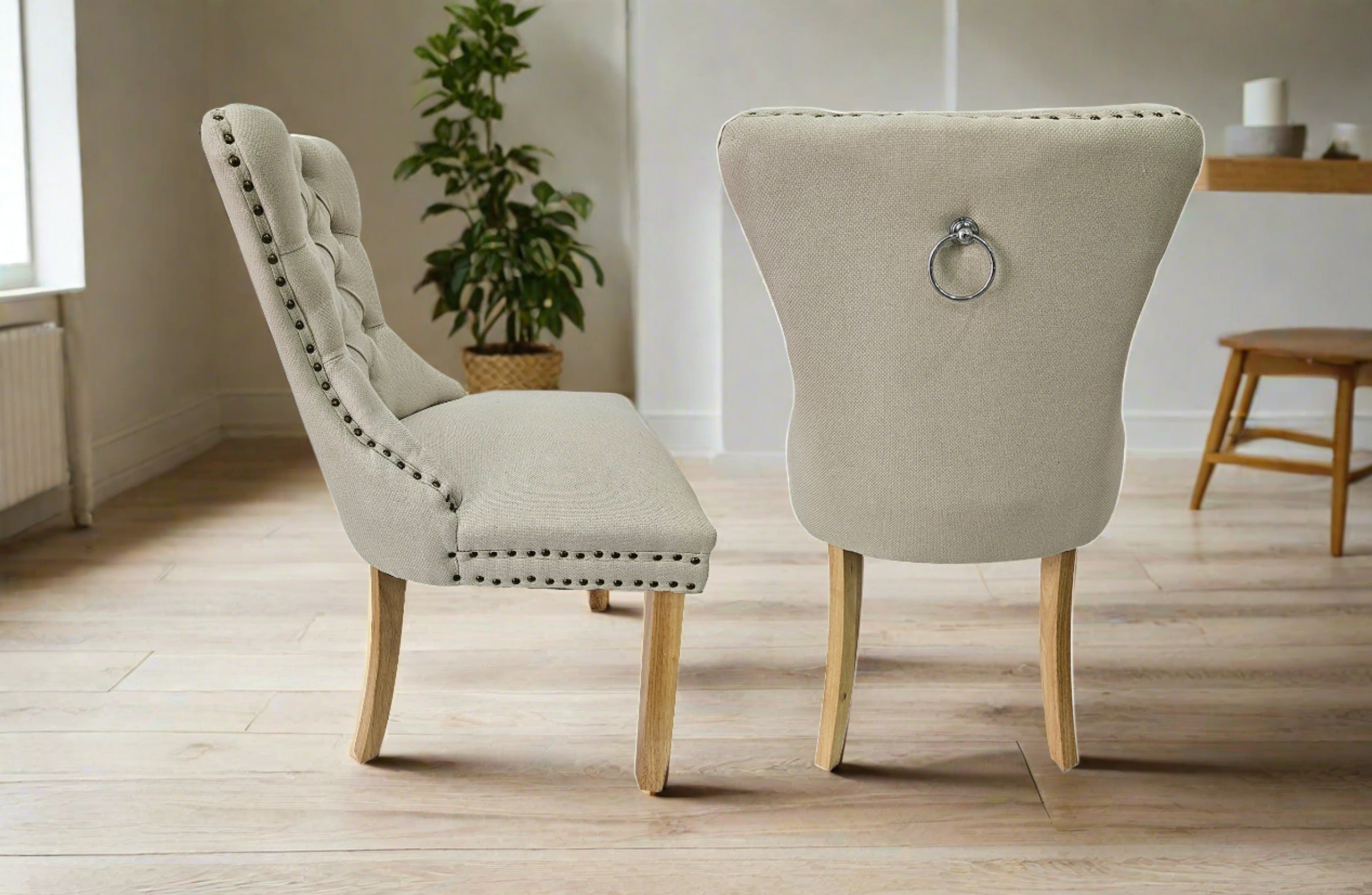 Alsea beige upholstered dining chairs with stud trim, tufted back, and ring handle in modern dining room setting.