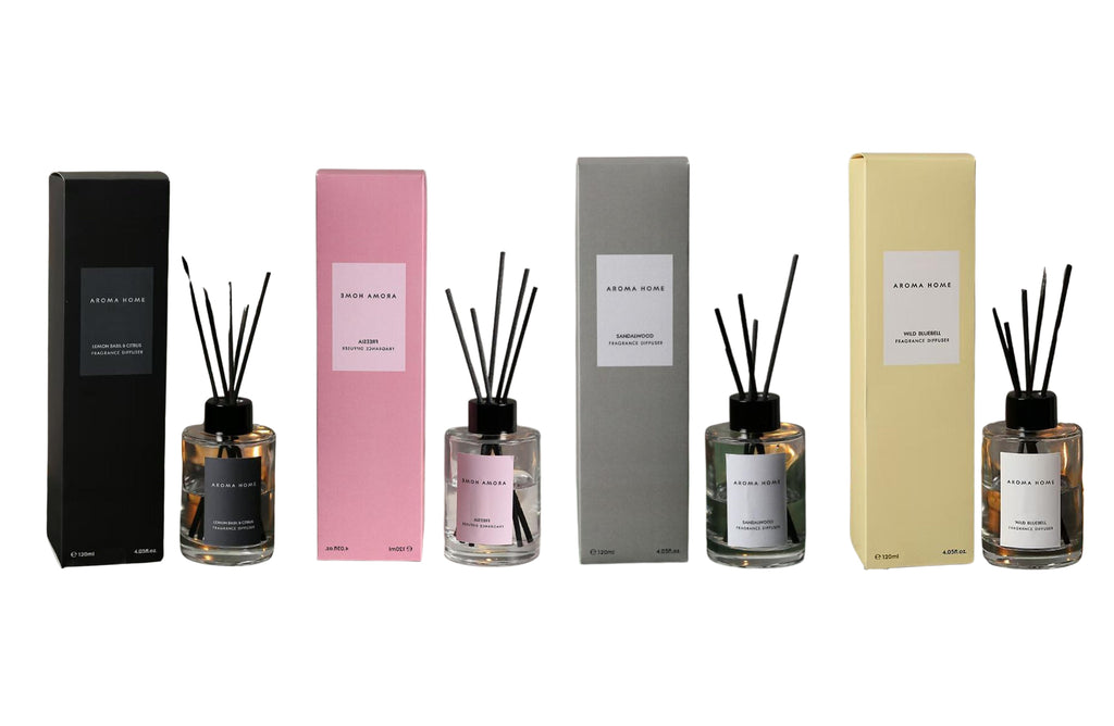 A lineup of four Aroma Diffuser 120ml bottles with matching color-coded boxes in black, pink, grey, and yellow, representing the scents: Sandalwood, Freesia, Wind Bluebell, and Lemon Basil & Citrus. Elegant glass containers with black diffuser reeds arranged beside each box.