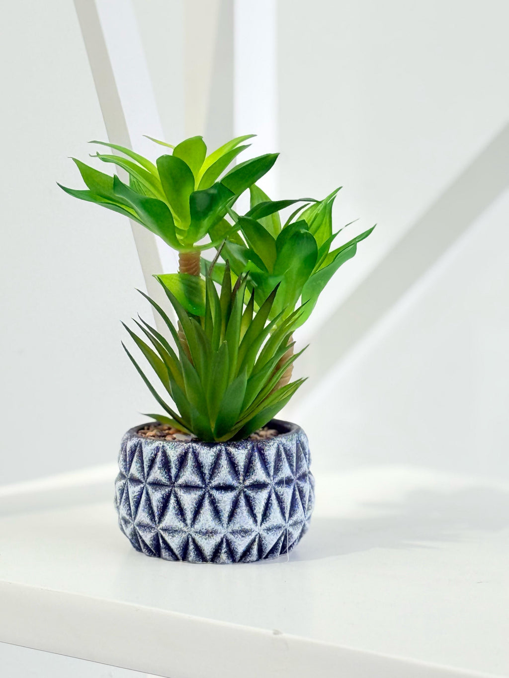 Faux succulent in a decorative diamond-pattern pot styled elegantly on a white surface.