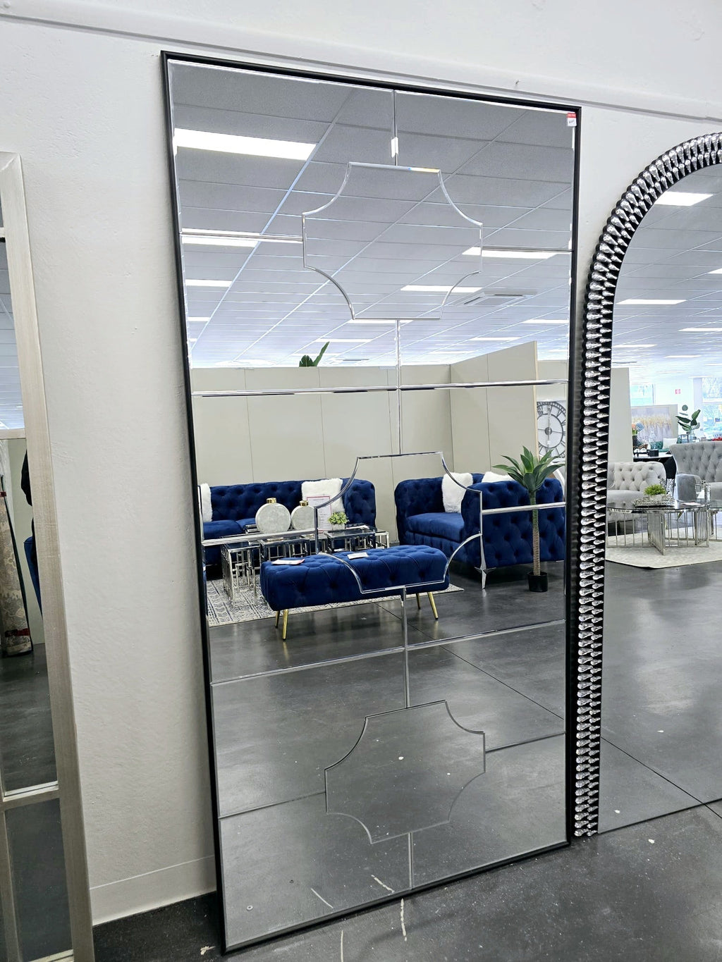 Mia Bevel extra large full length mirror styled in showroom with tufted blue sofas and décor.