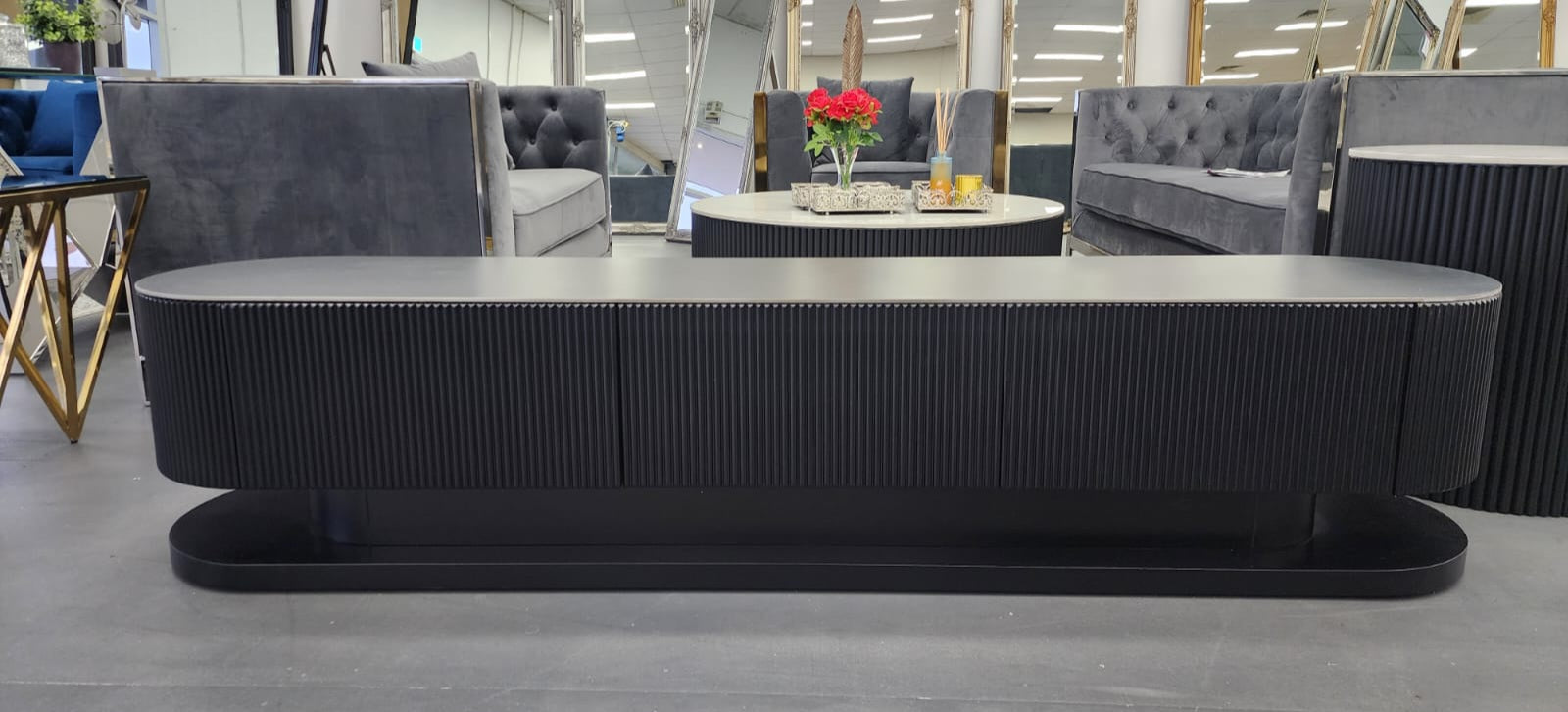 Black ripple TV unit styled in showroom with sofas and décor accents
