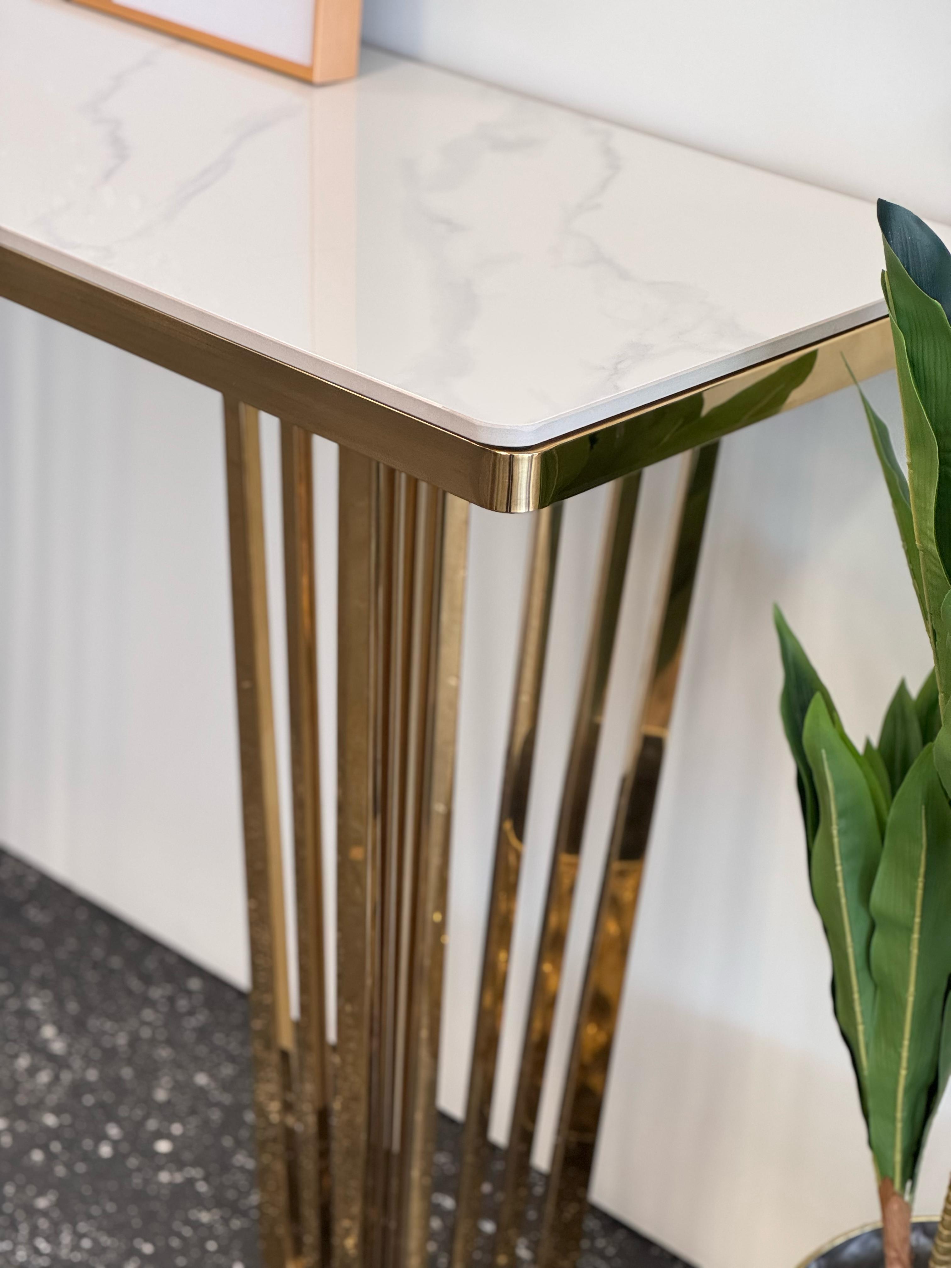Close-up of Serena console table with polished gold frame and white marble top beside plant.