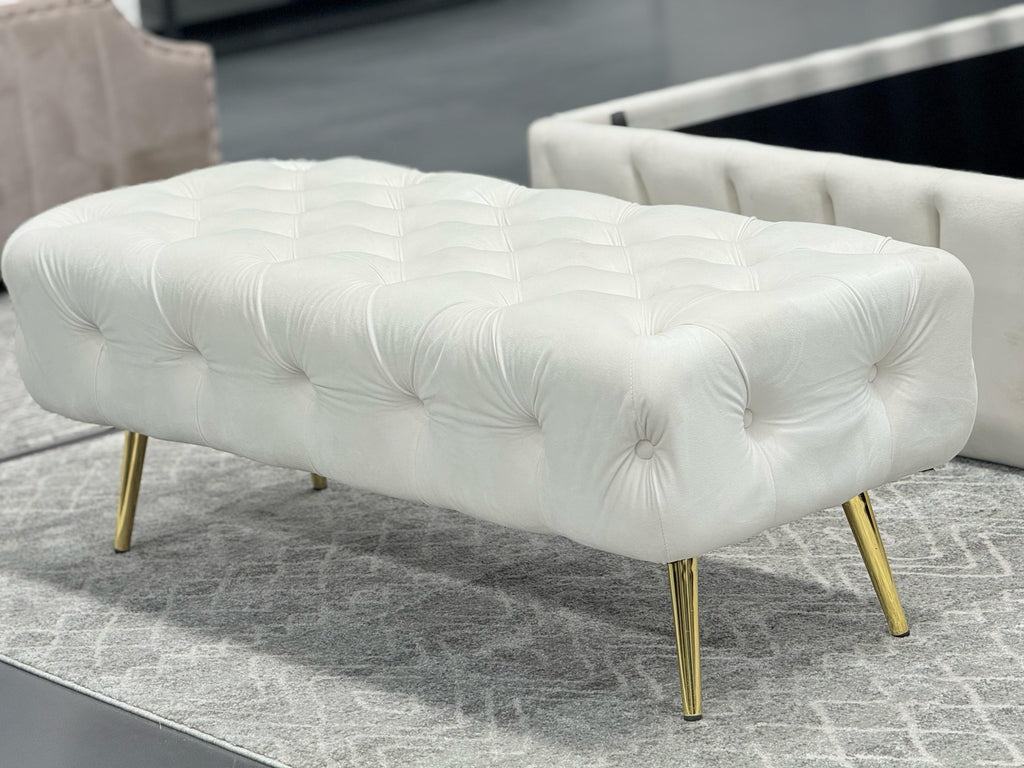 Beige Shirley Ottoman with gold legs, tufted velvet design, styled in modern living room.